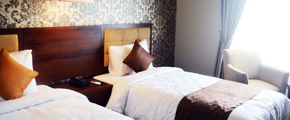 A hotel room with two beds, a wooden headboard, a nightstand with a phone, and a chair.
