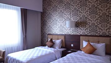 A hotel room with two beds, a nightstand, a lamp, and a chair.