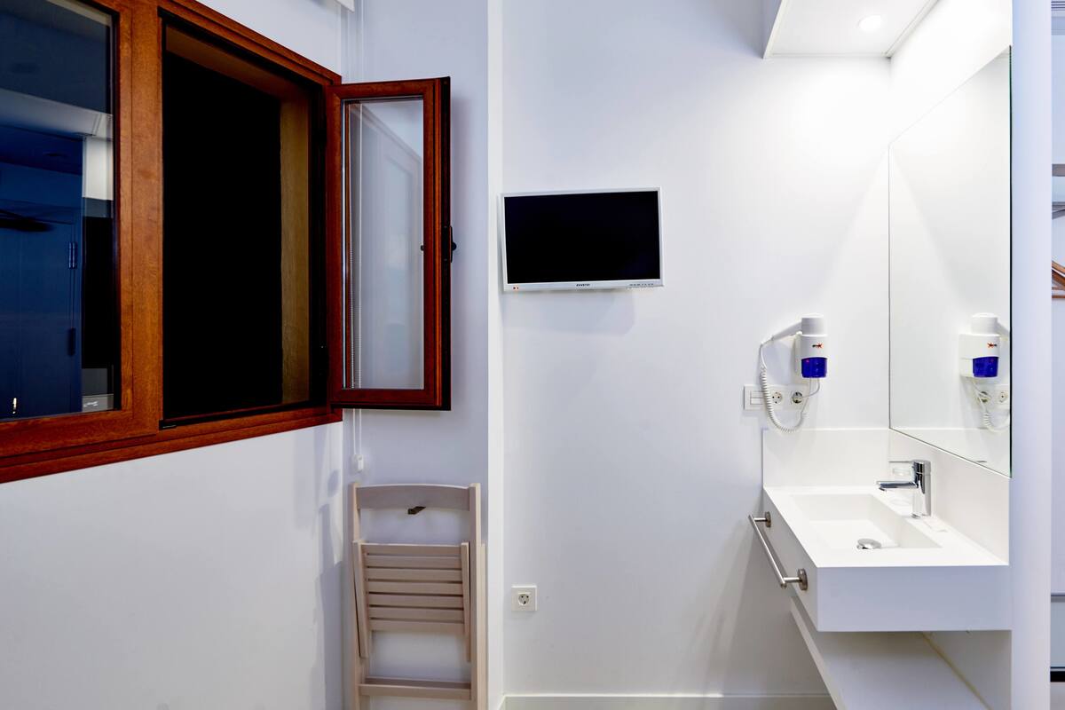 A modern bathroom with a wooden-framed window, a mounted television, and a white sink with a mirror.