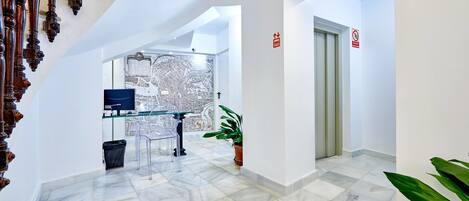 A modern hotel lobby with a marble floor, a map on the wall, a glass table with chairs, and a potted plant.