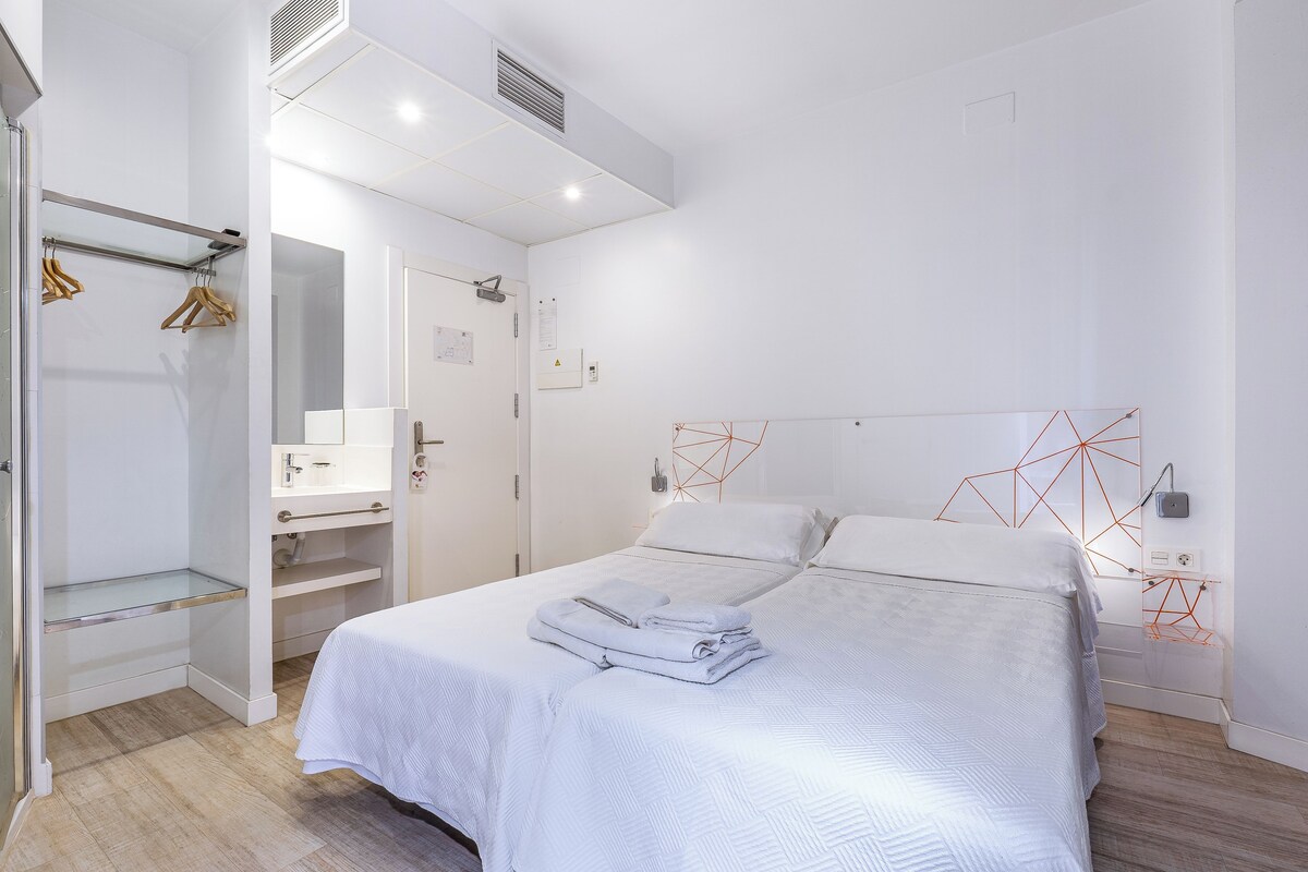 A modern bedroom with a neatly made bed, a walk-in closet, and a geometric wall decoration.