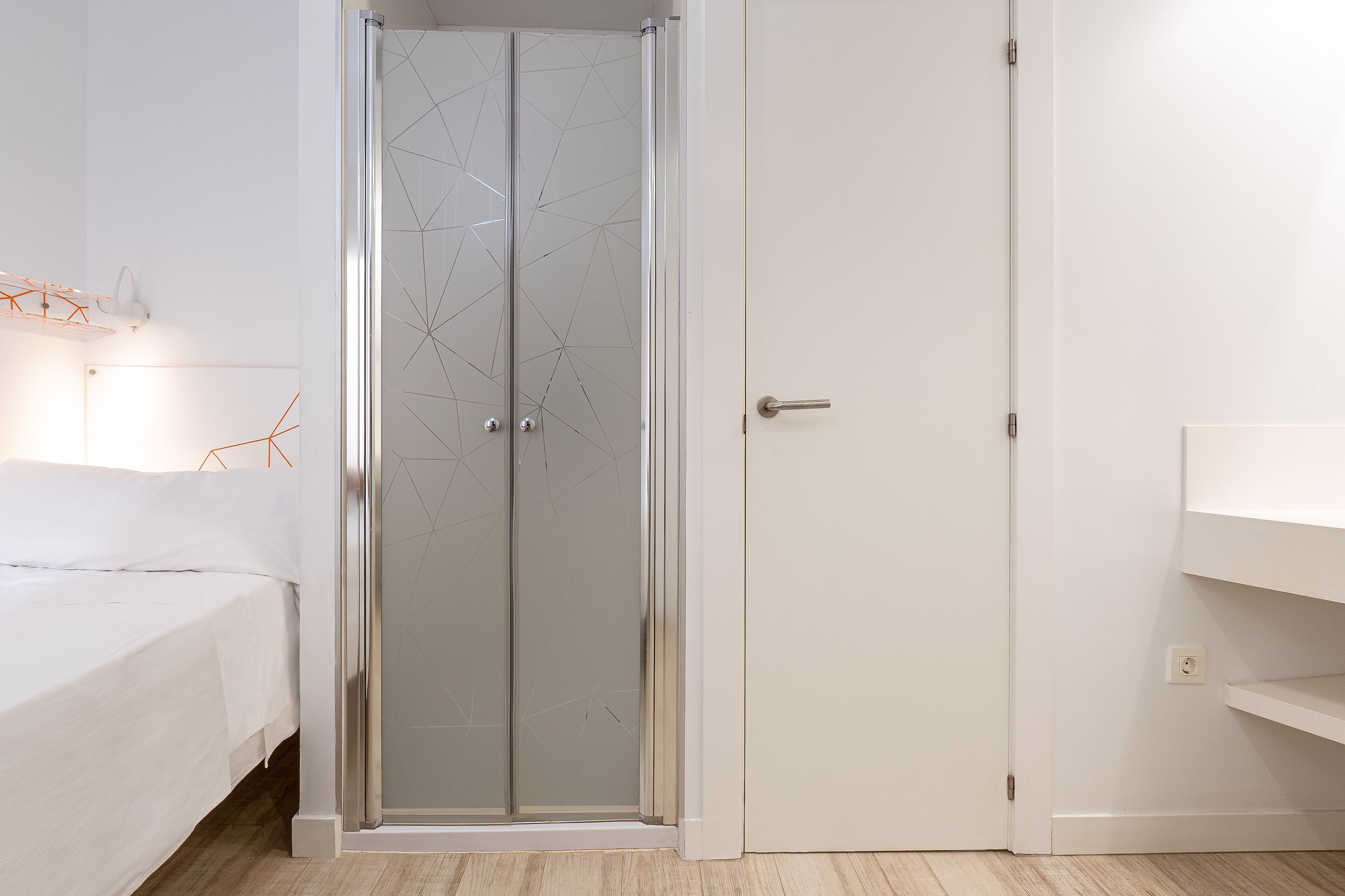 Un dormitorio con una cama, un armario blanco y cabina de ducha de vidrio.
