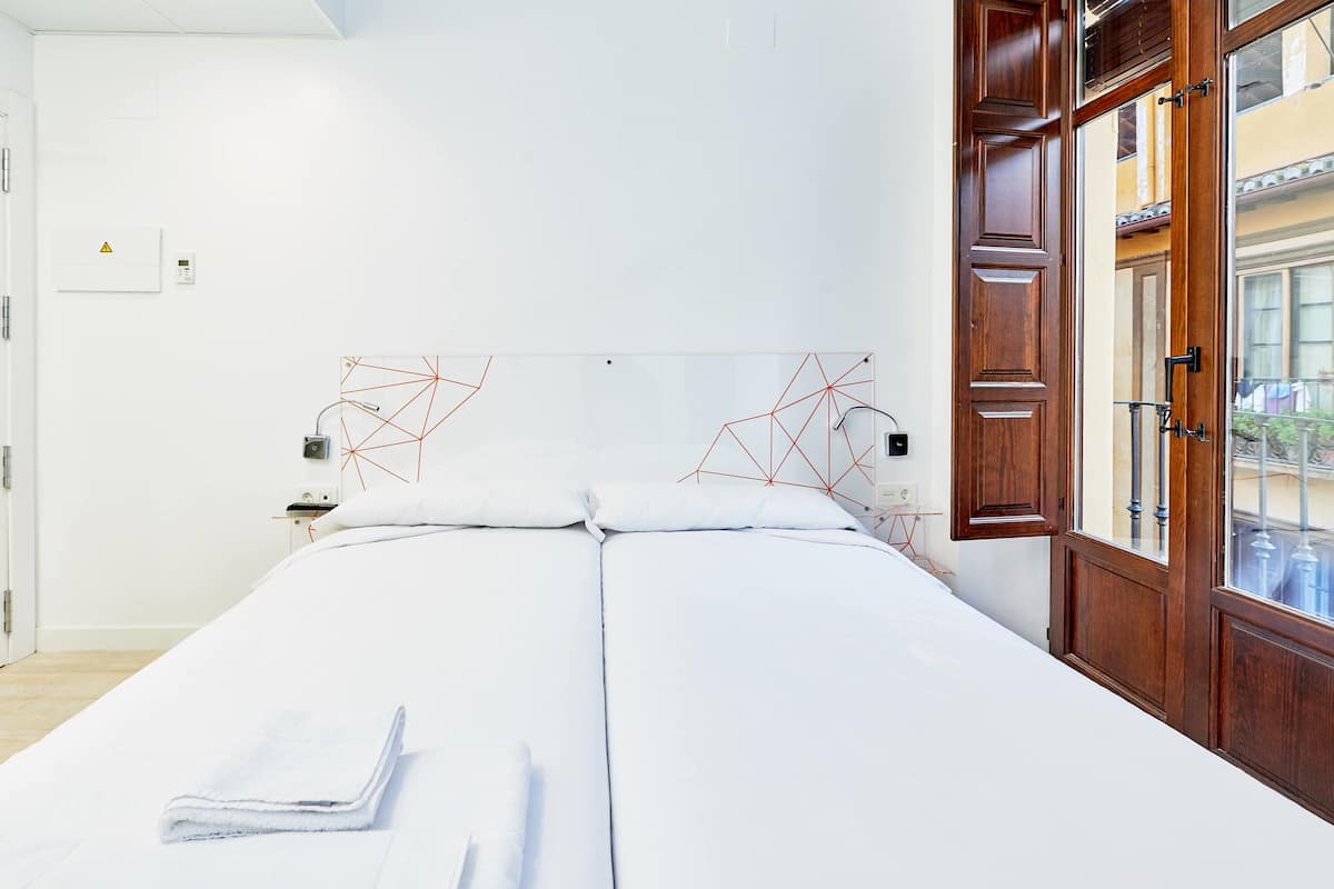 A hotel room with a bed, a wooden door, and a view of the outside.