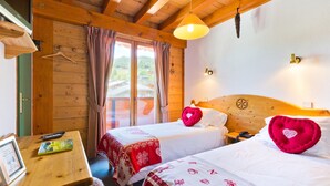 Habitación con dos camas, paredes y techo de madera, una mesa con un control remoto y una ventana con cortinas.
