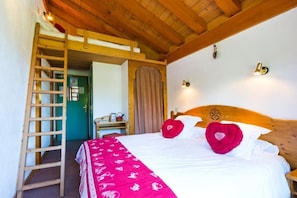 A bedroom with a bunk bed, a wooden ladder, a bed with white linens and red pillows, a wooden headboard, and a small bedside table. - Chalet Hôtel Aiguille Blanche (Les Gets)