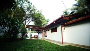 A courtyard with a white building, a covered seating area, and a lawn. - Summer Dew Villa (Unawatuna)