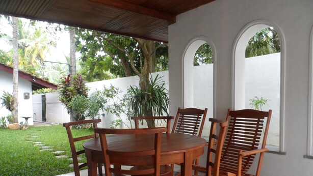 A patio with a round wooden table and six wooden chairs, surrounded by white walls and arched windows. - Summer Dew Villa (Unawatuna)