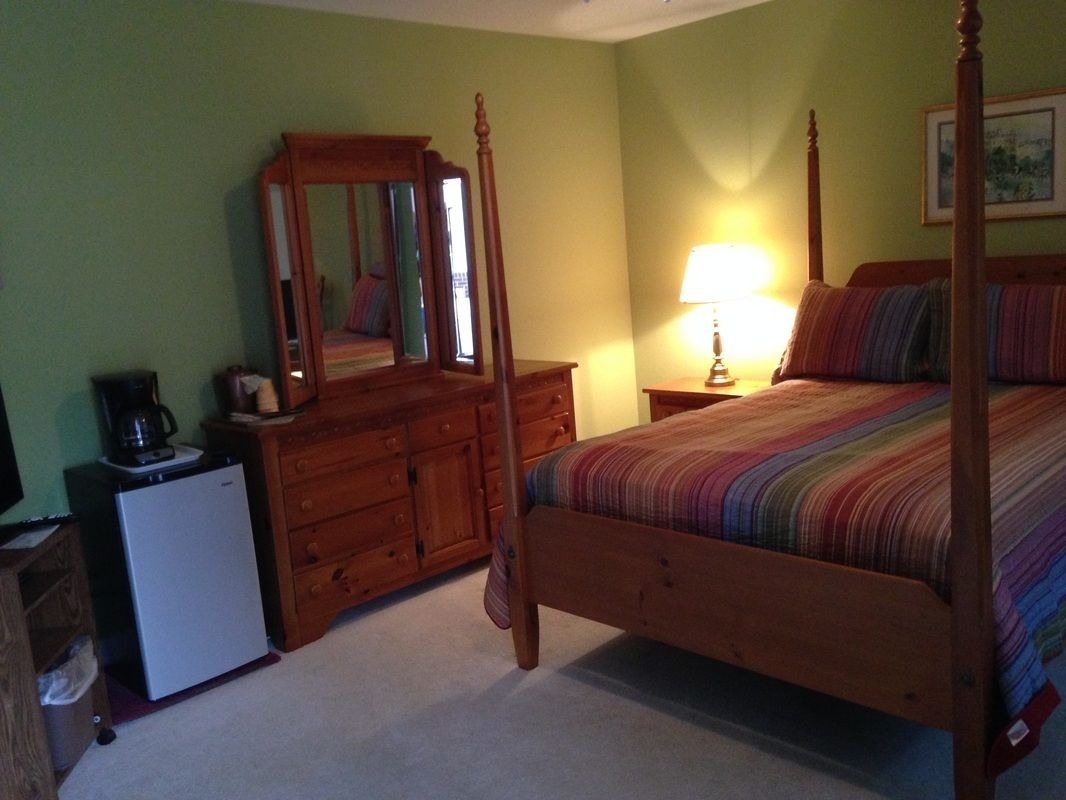 A bedroom with a four-poster bed, a dresser, a mirror, and a bedside lamp.