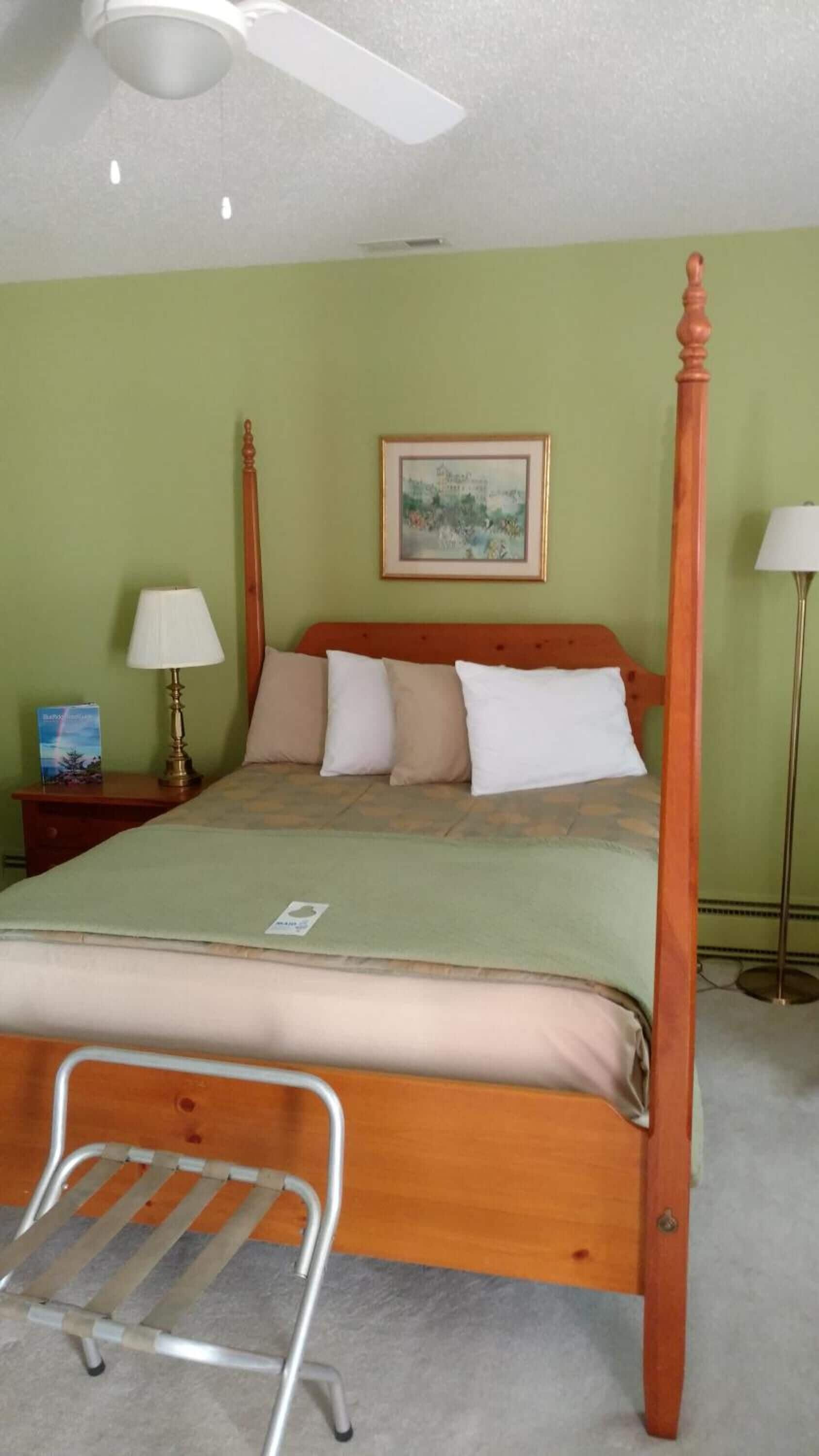 A four-poster bed with a headboard, a bedside table with a lamp, and a framed picture on the wall.