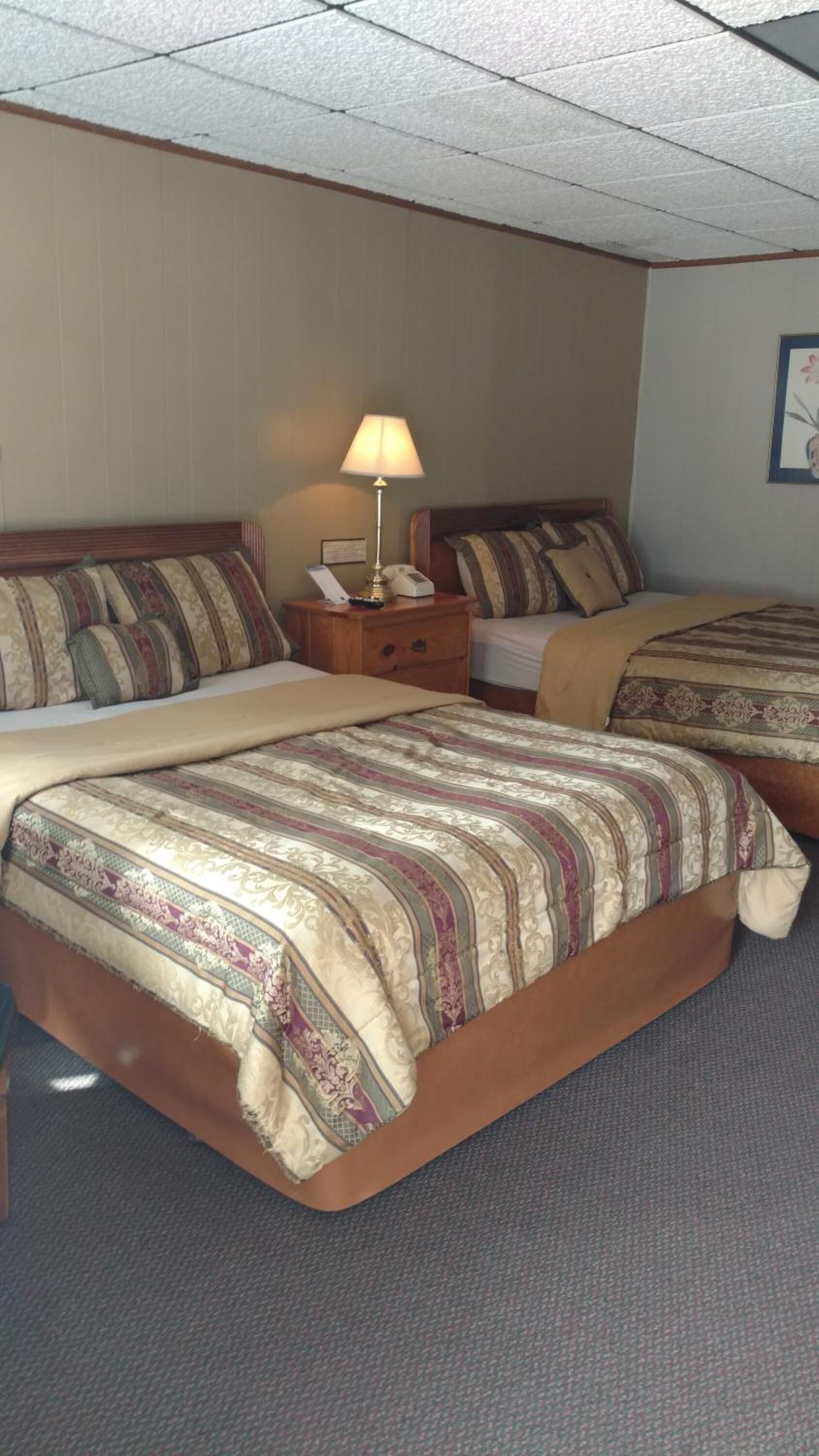 A hotel room with two beds, a nightstand with a lamp, and a framed picture on the wall.