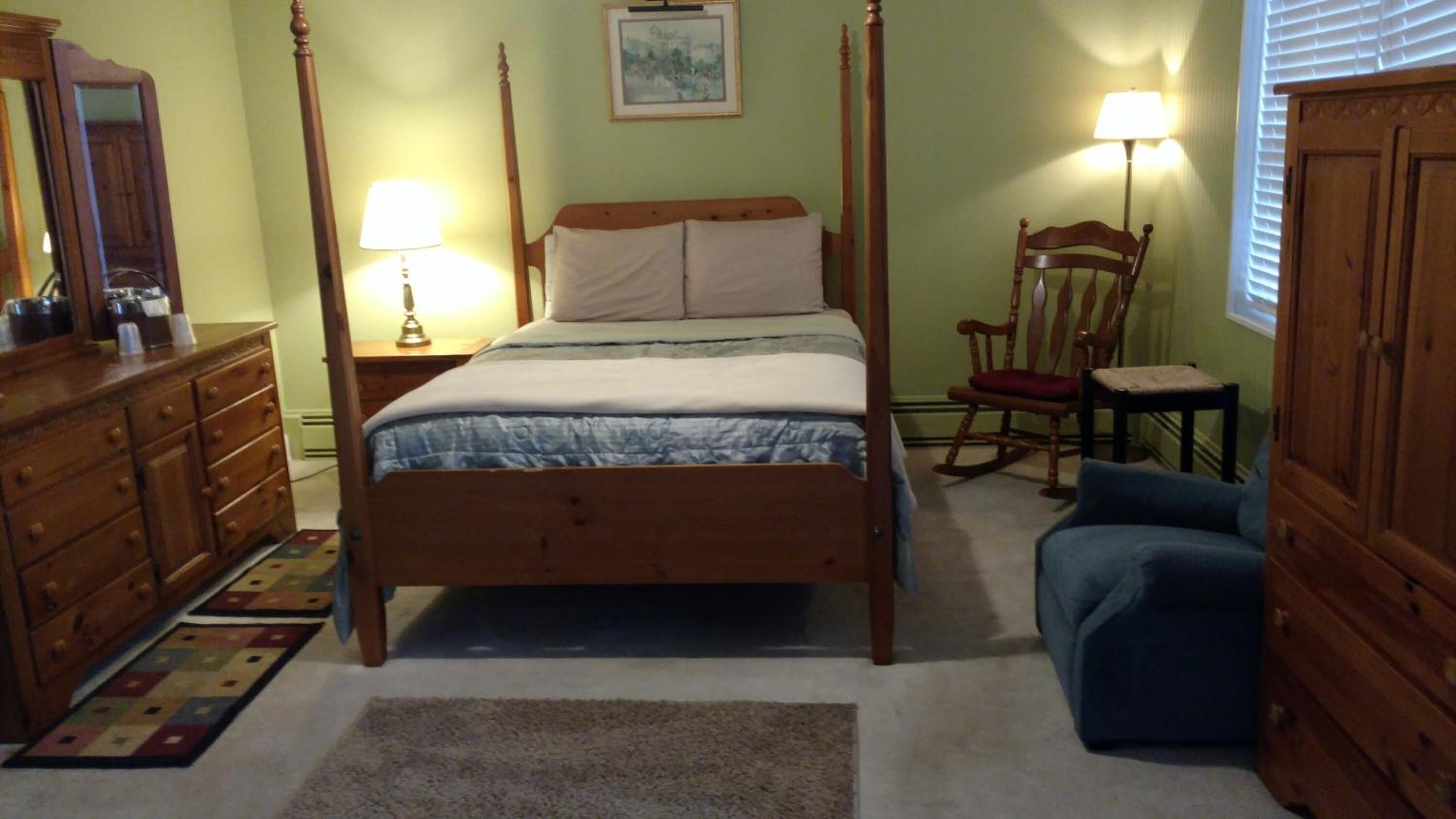 A bedroom with a four-poster bed, a dresser, a chair, and a lamp.