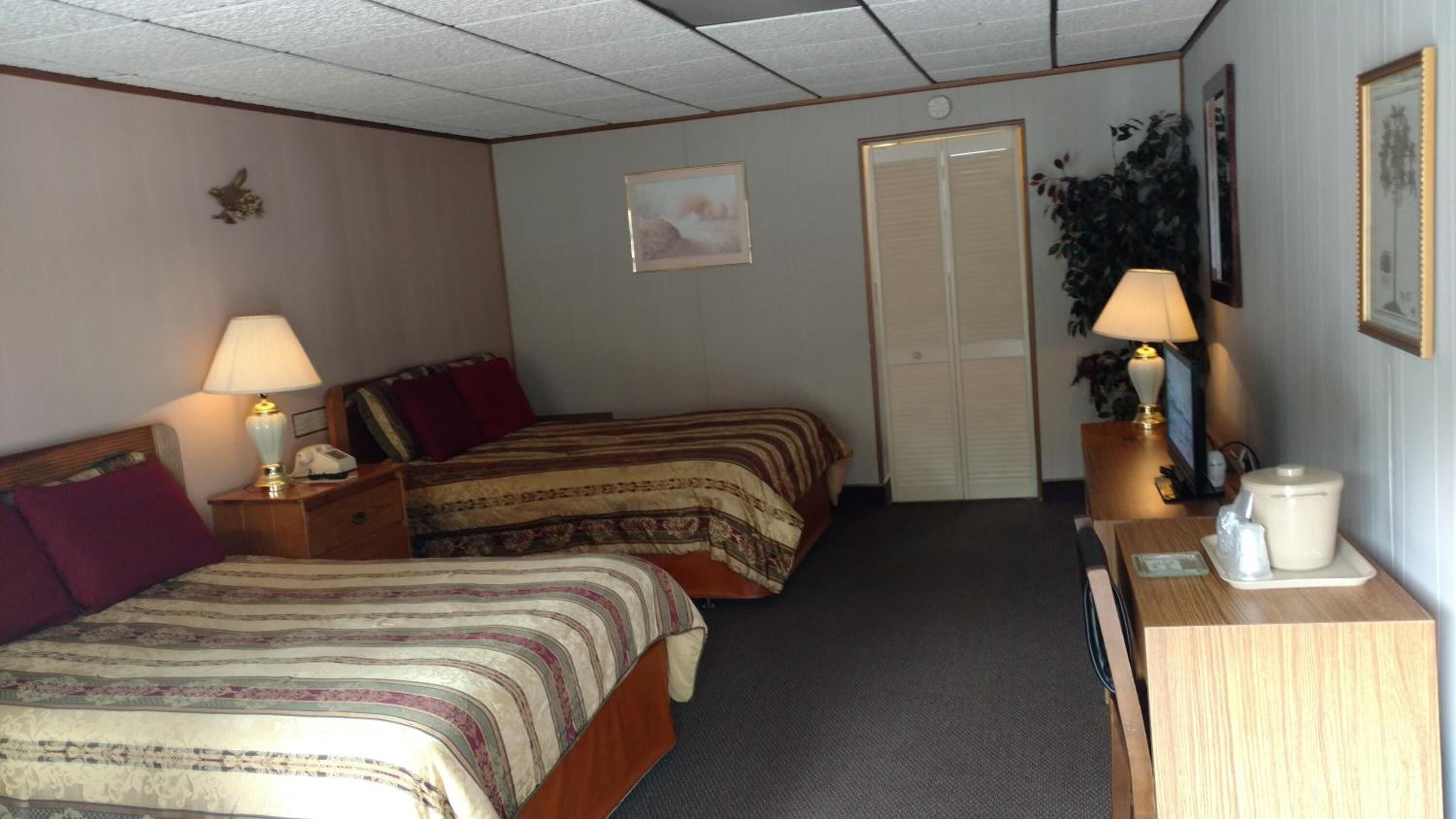A hotel room with two beds, a desk, a chair, a lamp, a coffee maker, and a door.