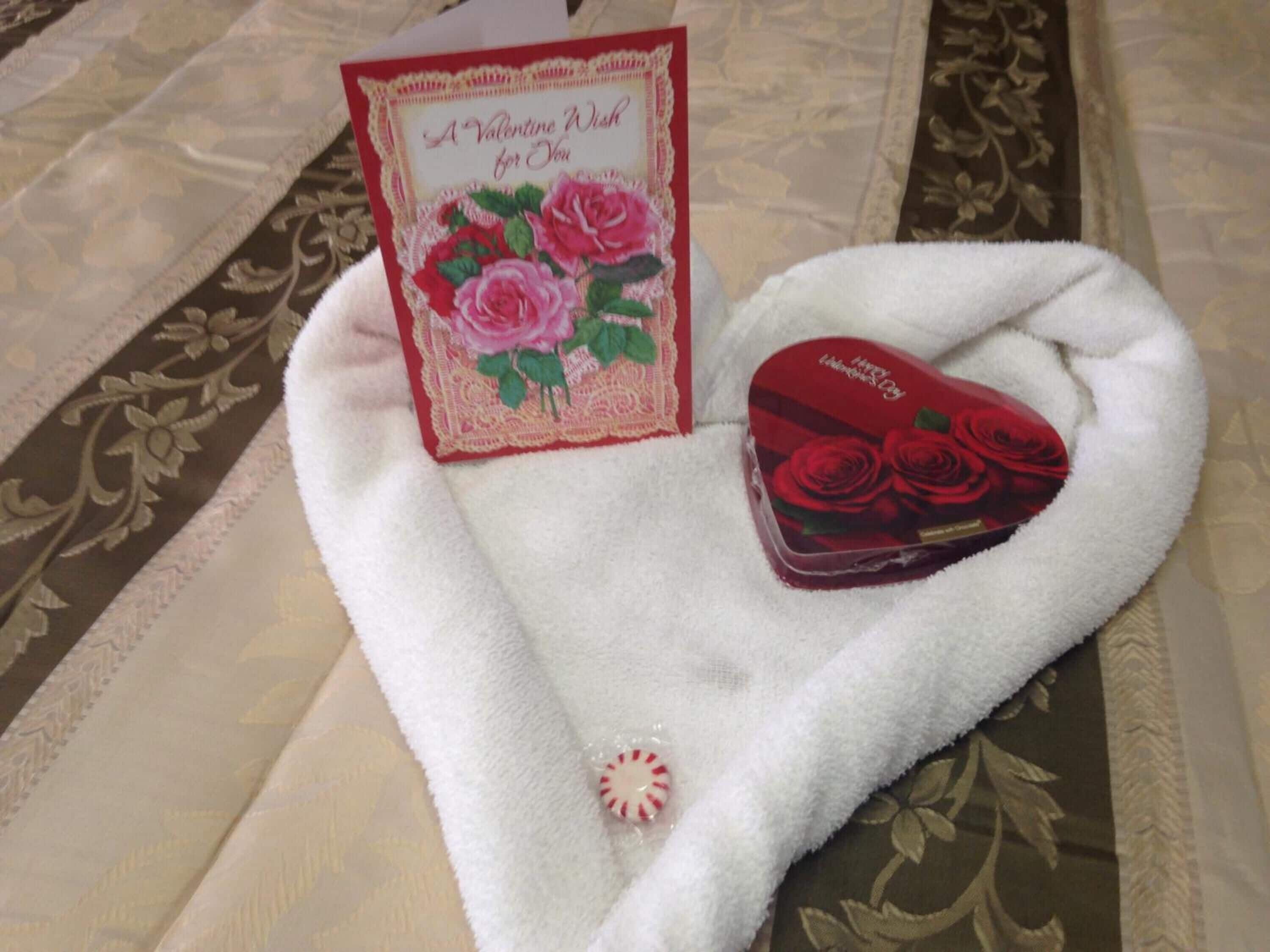 A white towel with a heart-shaped box and a Valentine's Day card on a patterned fabric.