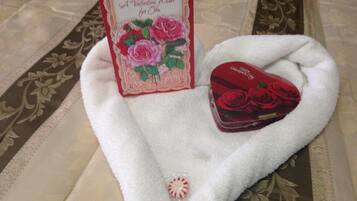 A white towel with a heart-shaped box and a Valentine's Day card on a patterned fabric.