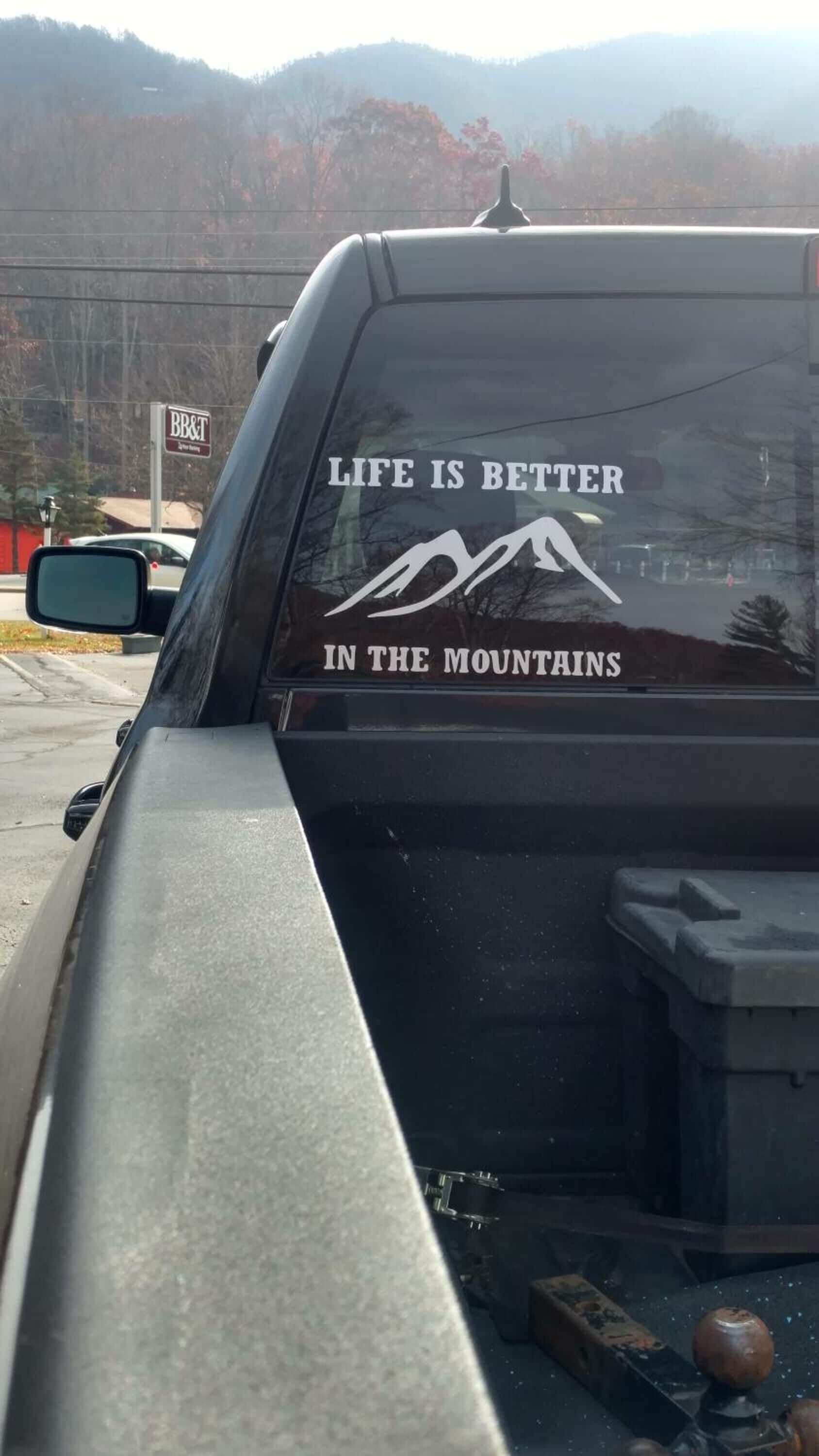 A vehicle with a rear window decal stating "LIFE IS BETTER IN THE MOUNTAINS" and a mountain graphic.