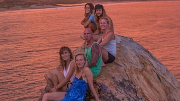 A group of people sitting on a rock by a body of water during sunset.