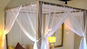 Una habitación con una cama bajo un dosel, una mesita de noche con lámpara y un banco de madera.