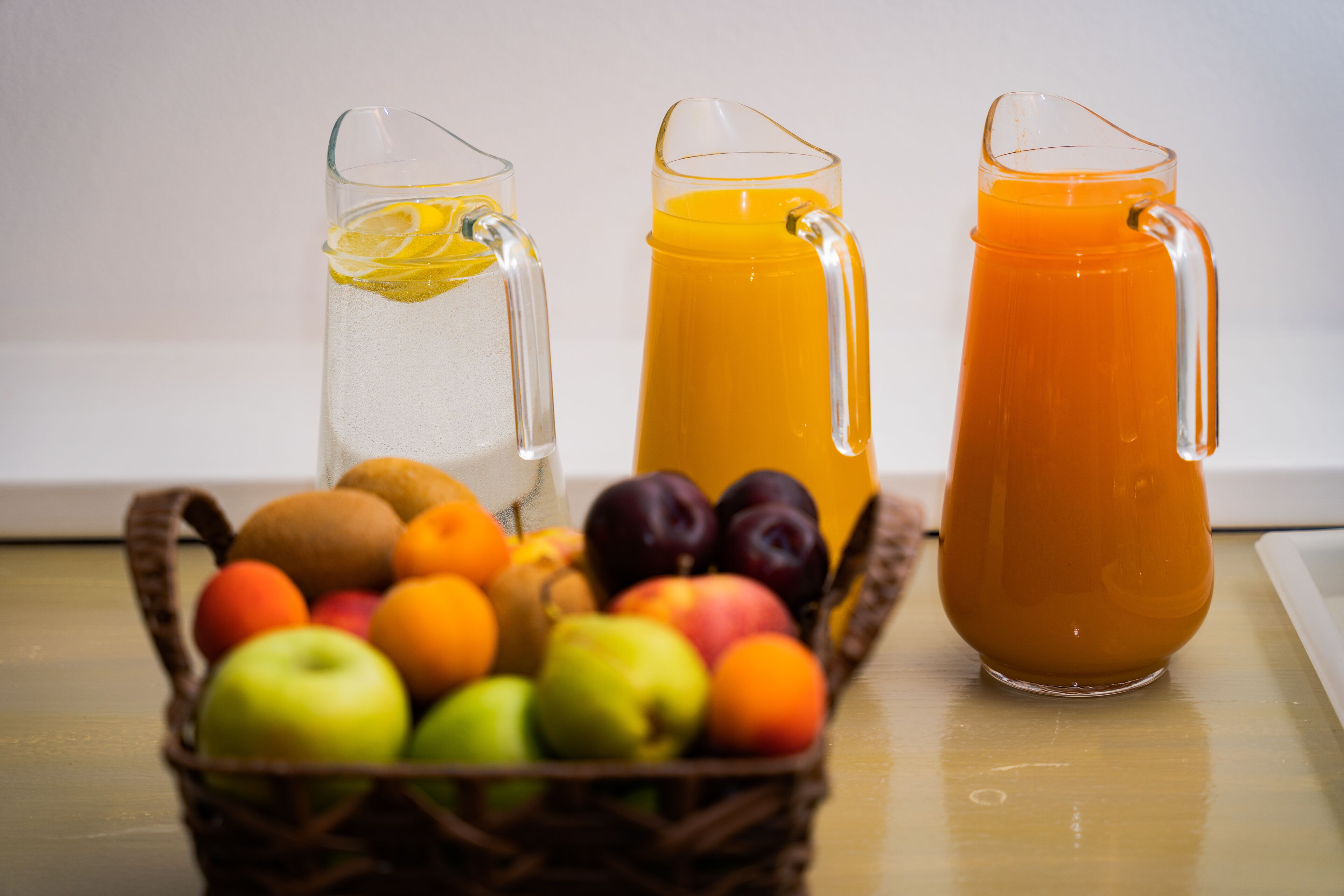 A table with a fruit basket and two pitchers of beverages.