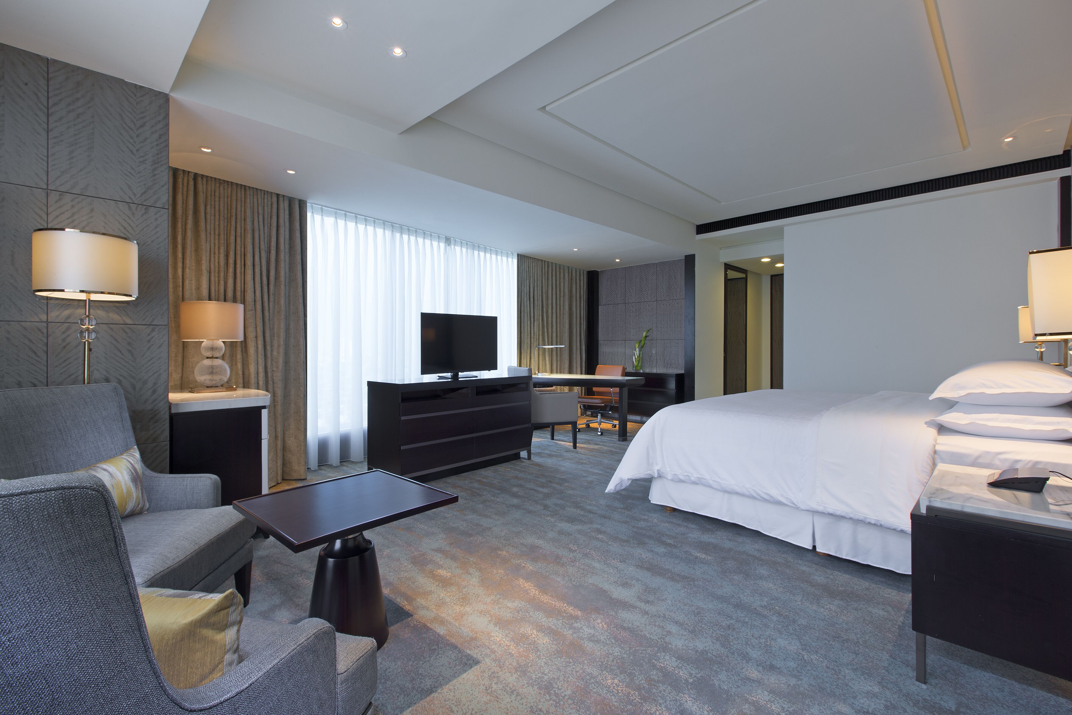Una moderna camera d'albergo con un letto grande, una scrivania, una televisione e un angolo relax con divano e poltrona.