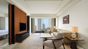 Habitación de hotel moderna con televisor grande, asientos cómodos, vista a la ciudad y decoración minimalista.