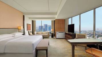 Habitación de hotel con una cama grande, un escritorio, una silla, un televisor y vistas de la ciudad.