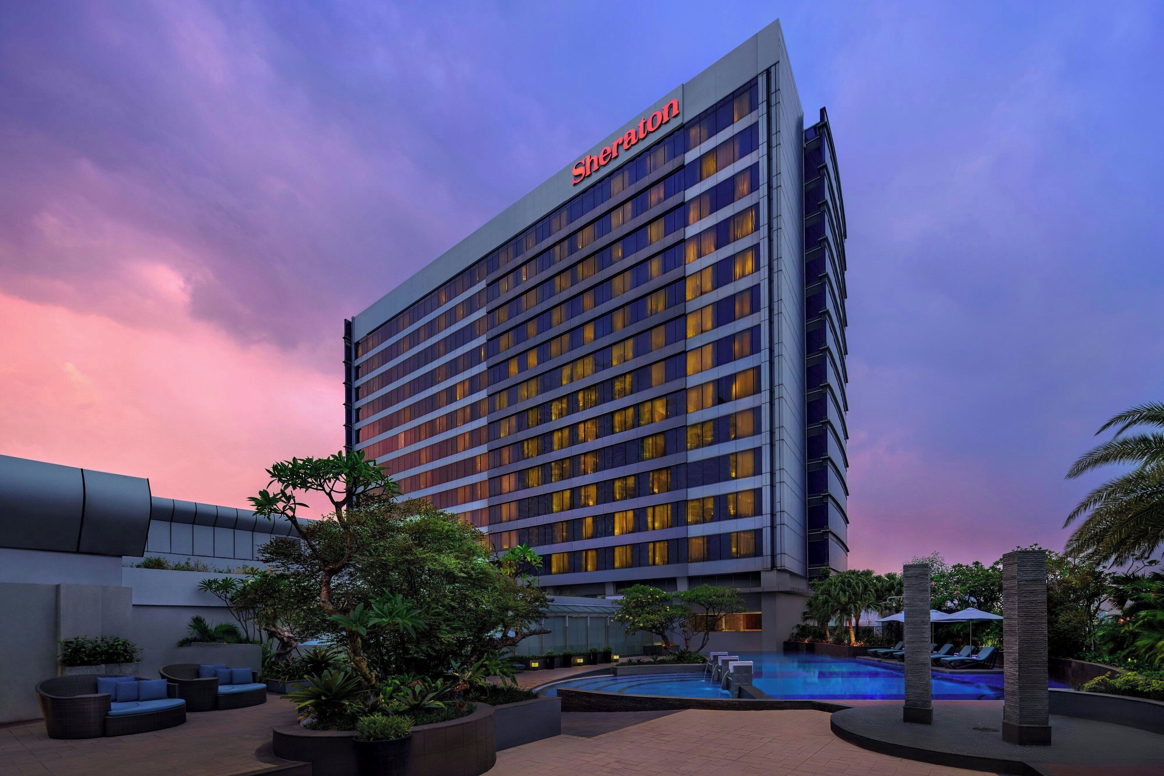 A Sheraton hotel with a pool area, outdoor seating, and a sunset sky.