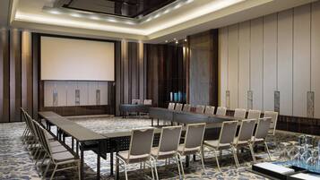 A conference room with a long table, chairs, a projector screen, and a carpeted floor.