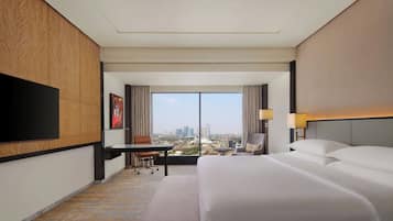 A hotel room with a large bed, a desk, a chair, a TV, and a view of the city.
