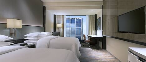 A hotel room with two beds, a desk, a chair, a TV, and a large window with a city view.