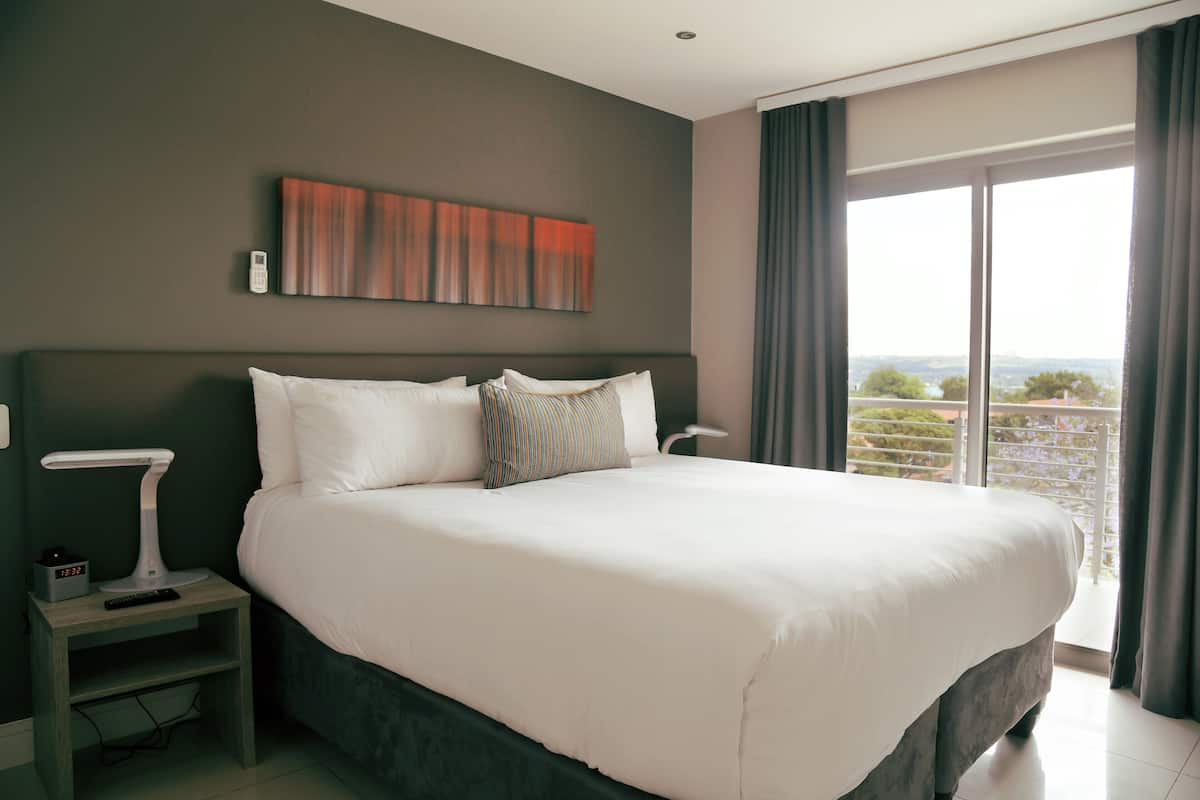 Een groot bed met witte lakens, een nachtkastje met een lamp en een schilderij aan de muur.
