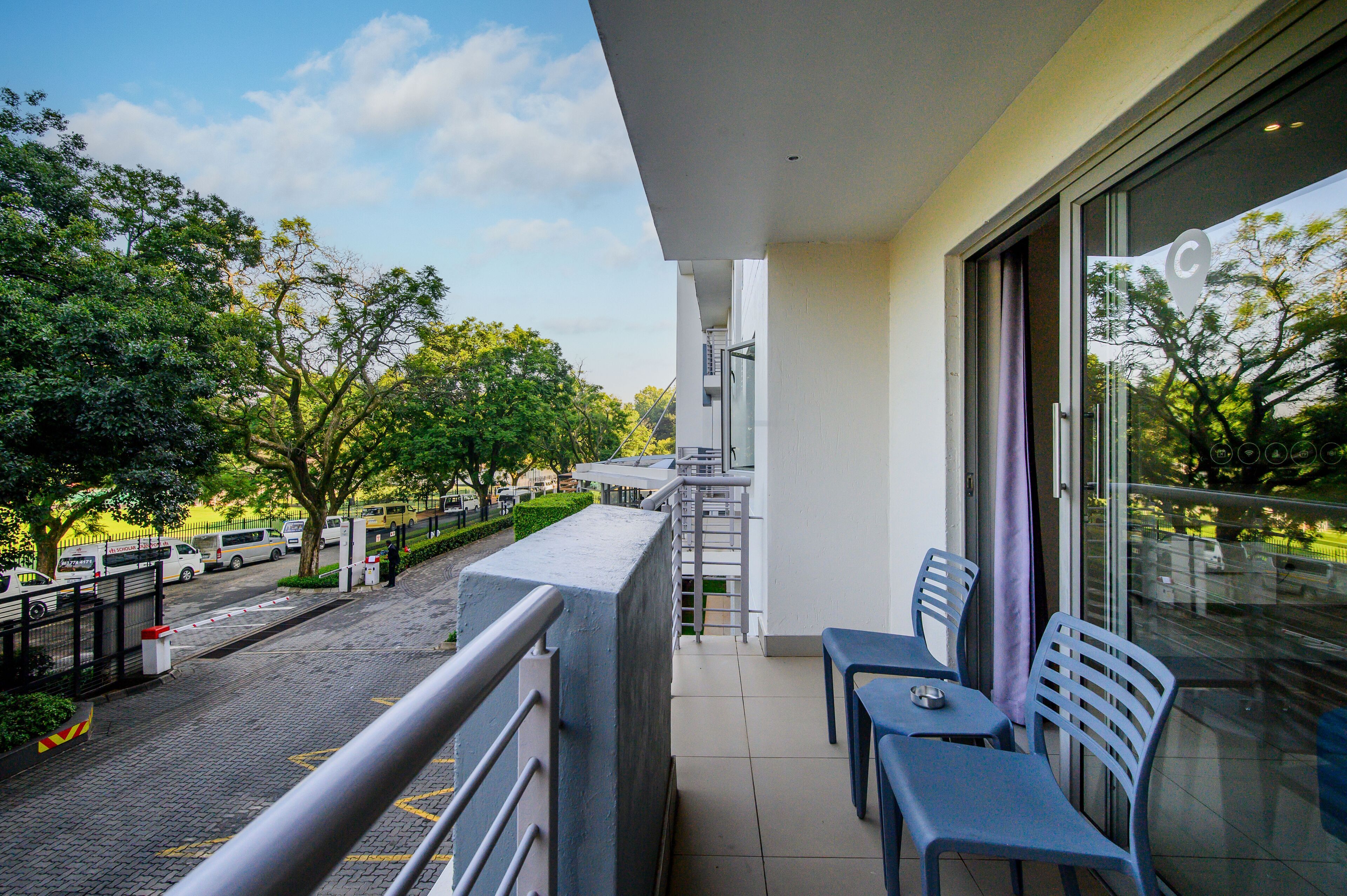 A balcony with two chairs and a table, overlooking a parking area and trees.