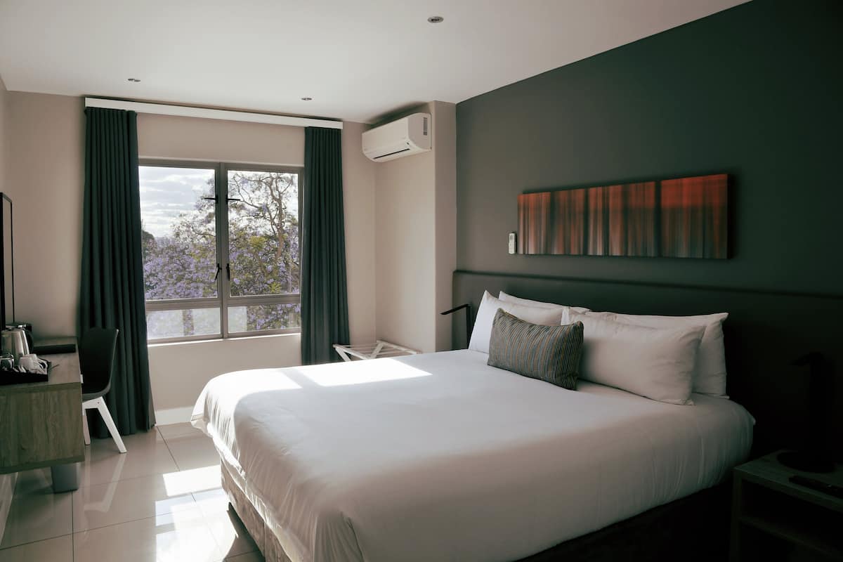 Een moderne hotelkamer met een groot bed, een bureau, een stoel en een raam met gordijnen.