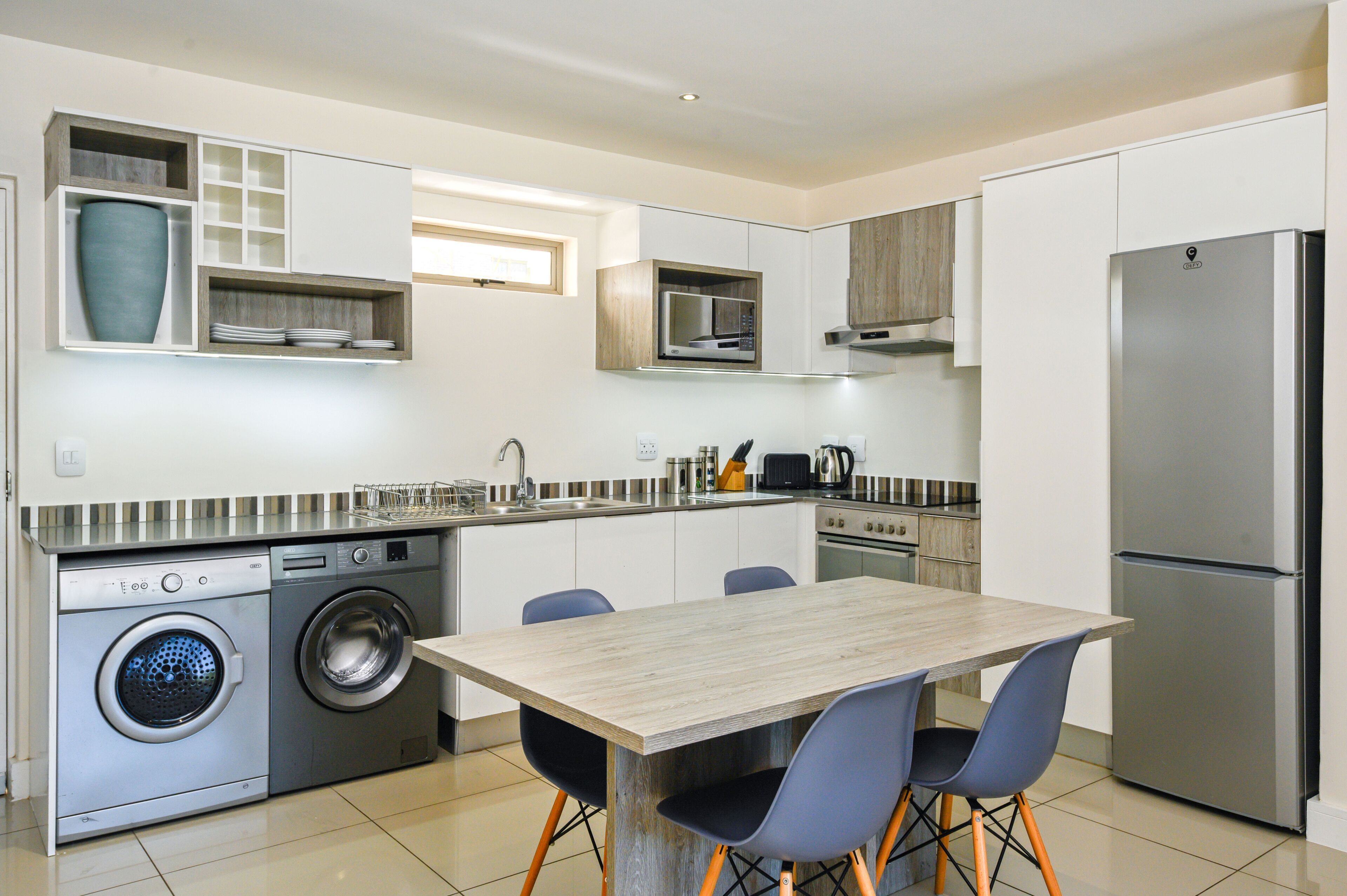 A modern kitchen with built-in appliances, a dining area with a wooden table and chairs, and a washing machine.