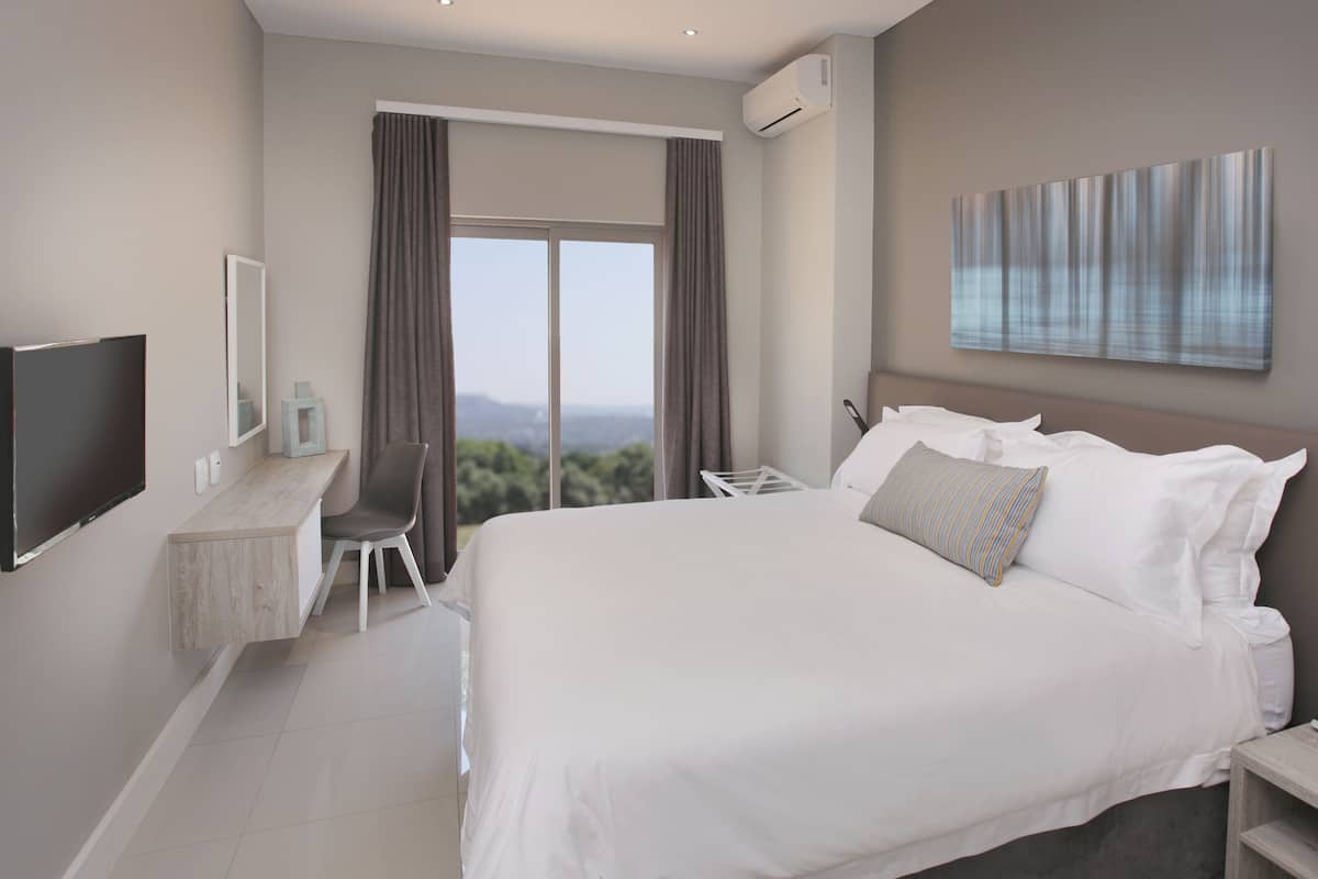 Een moderne hotelkamer met een groot bed, een bureau met stoel, een flatscreen televisie en een groot raam met gordijnen.