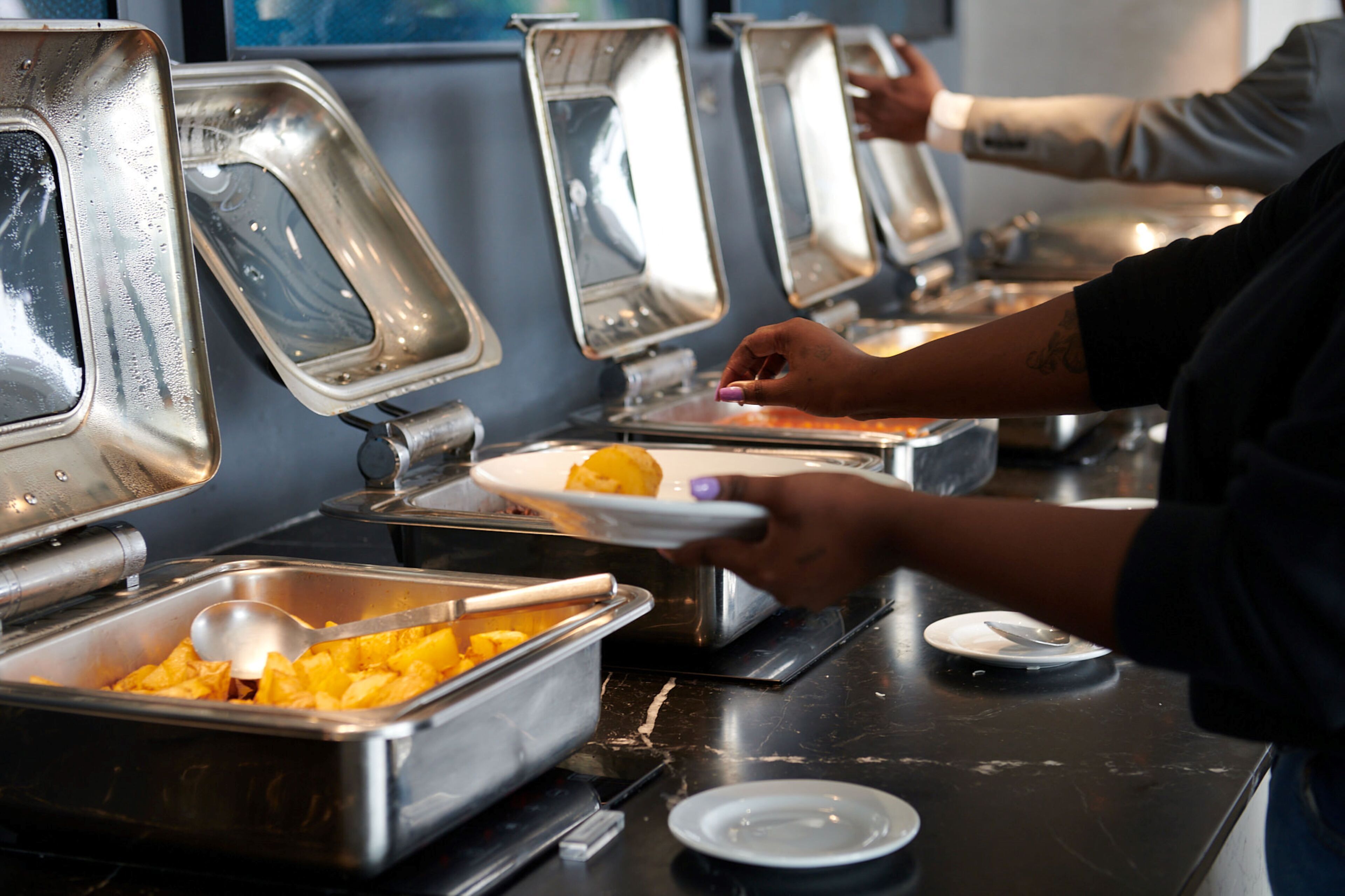 Een buffet met meerdere food stations, waaronder een schaal met blokjes eten en een bakje dat waarschijnlijk aardappelpuree bevat.