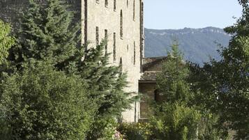 Un área de comedor al aire libre con un edificio de piedra al fondo, rodeada de vegetación.