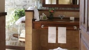 A bathroom with a stone wall, wooden vanity, a mirror, and a bench. - Casa de San Martín (Fiscal)