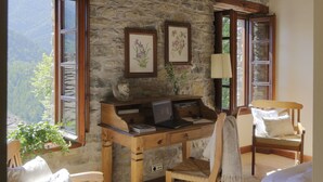 A rustic room with stone walls, wooden furniture, and a desk with a computer. There are windows offering a view of the mountains. - Casa de San Martín (Fiscal)