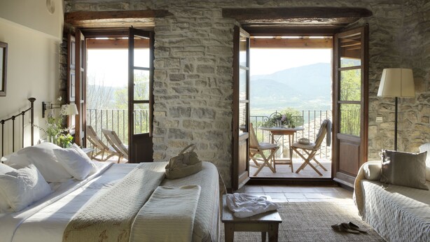 A cozy bedroom with a stone wall, a bed with white linens, a small table, and a chair. - Casa de San Martín (Fiscal)