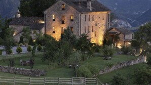 A stone building with multiple windows and a well-lit entrance, surrounded by a stone wall and greenery. - Casa de San Martín (Fiscal)