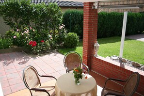 Un patio con dos sillas de mimbre, una mesa redonda con un jarrón de flores y un muro de ladrillo.