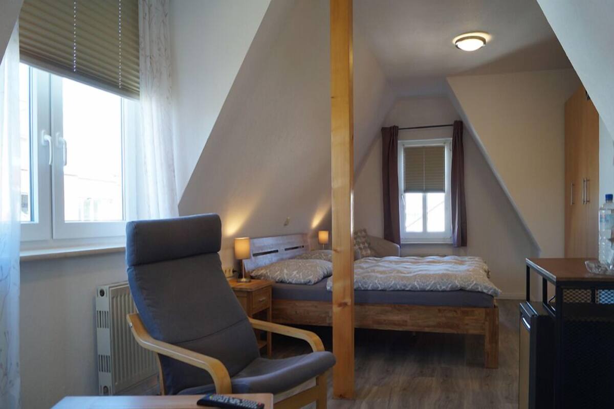 Une chambre mansardée chaleureuse, avec un lit, une chaise, une petite table et un radiateur.