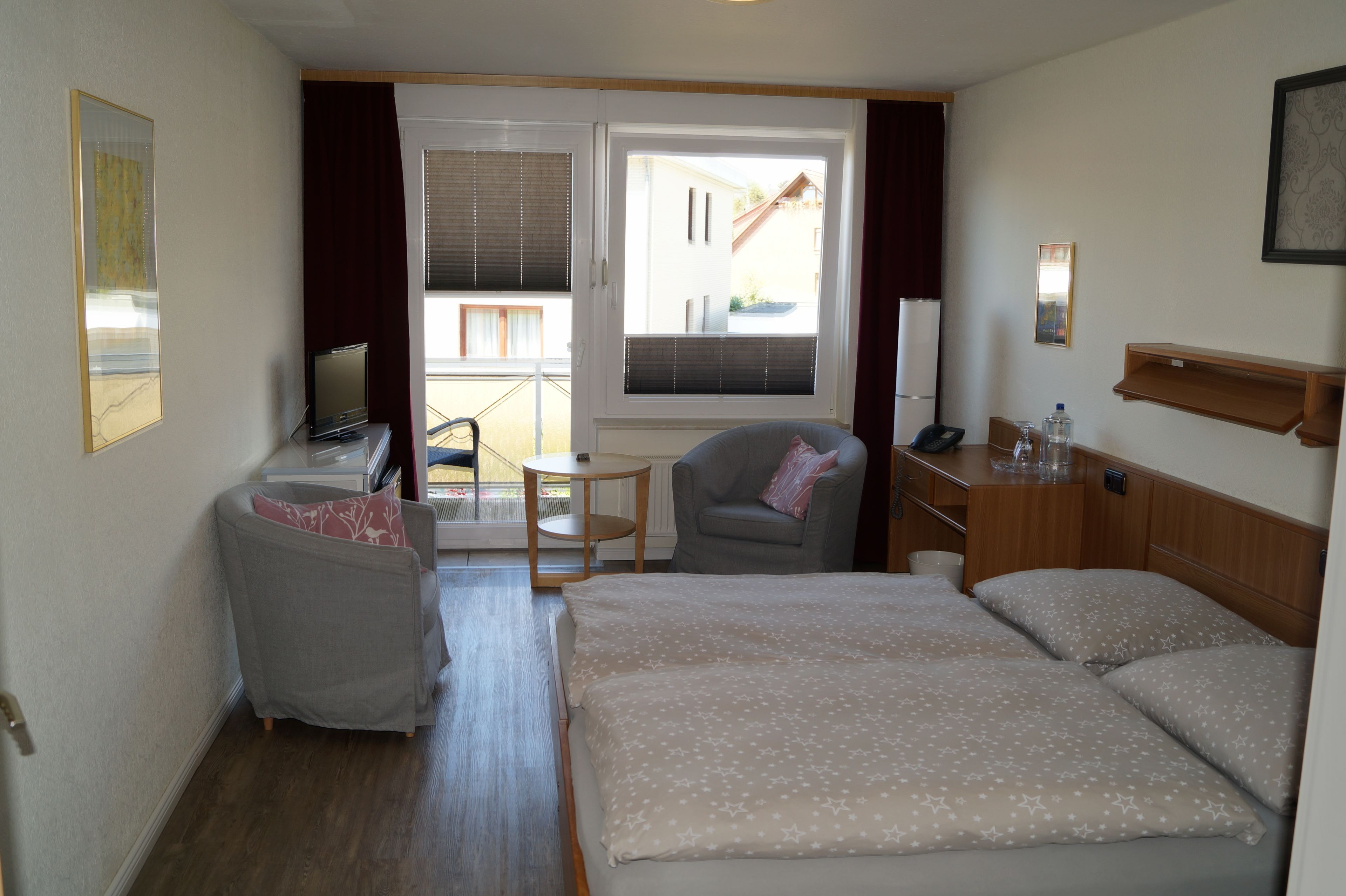 A hotel room with a bed, a desk, a chair, a TV, and a view of the outside.