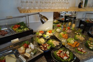 Un bufé con diversas opciones de comida, incluyendo ensaladas, quesos y carnes.
