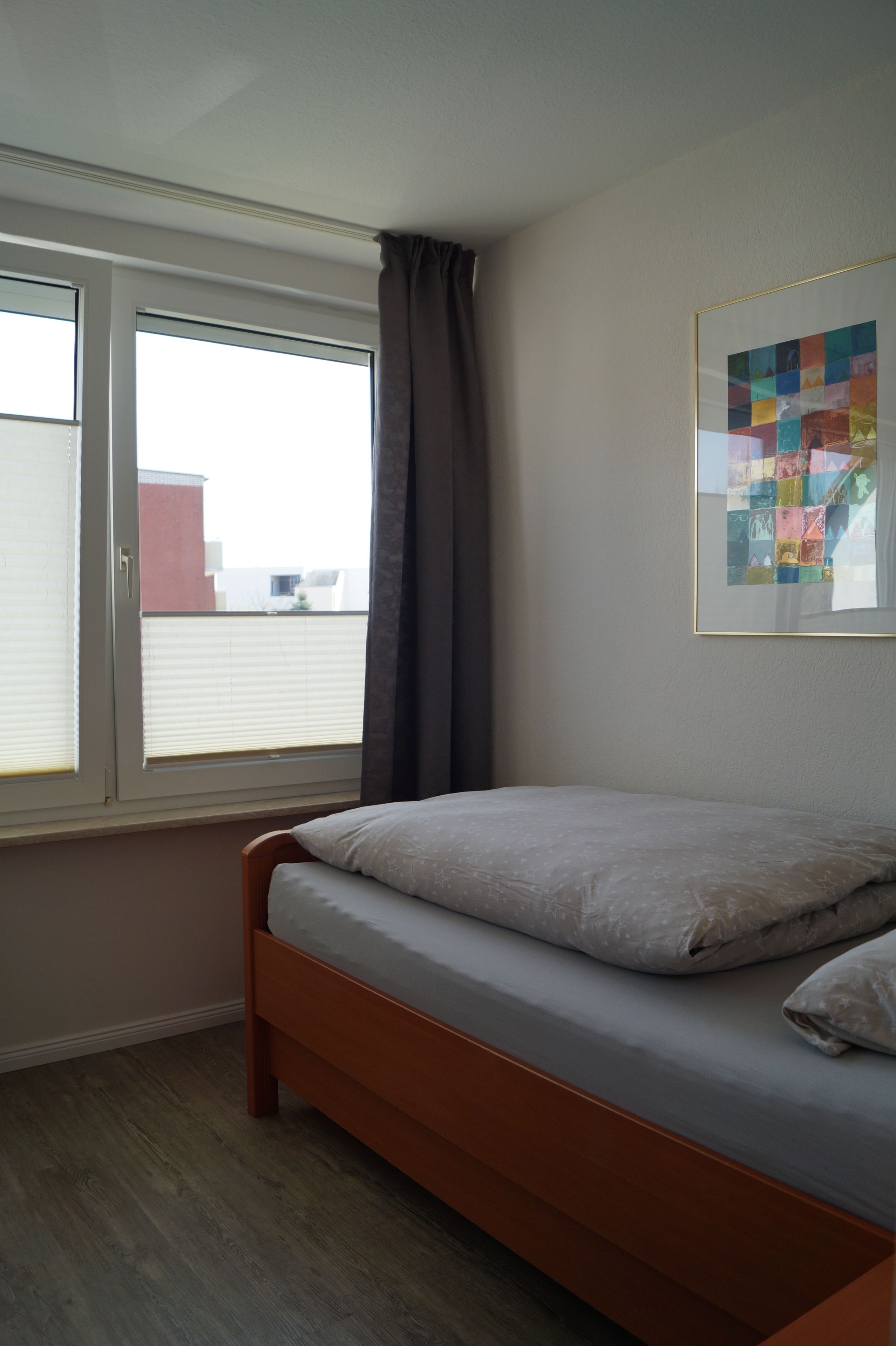 Ein Schlafzimmer mit einem Bett, einem Fenster mit Vorhängen und einem gerahmten Bild an der Wand.
