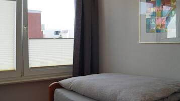 Ein Schlafzimmer mit einem Bett, einem Fenster mit Vorhängen und einem gerahmten Bild an der Wand.