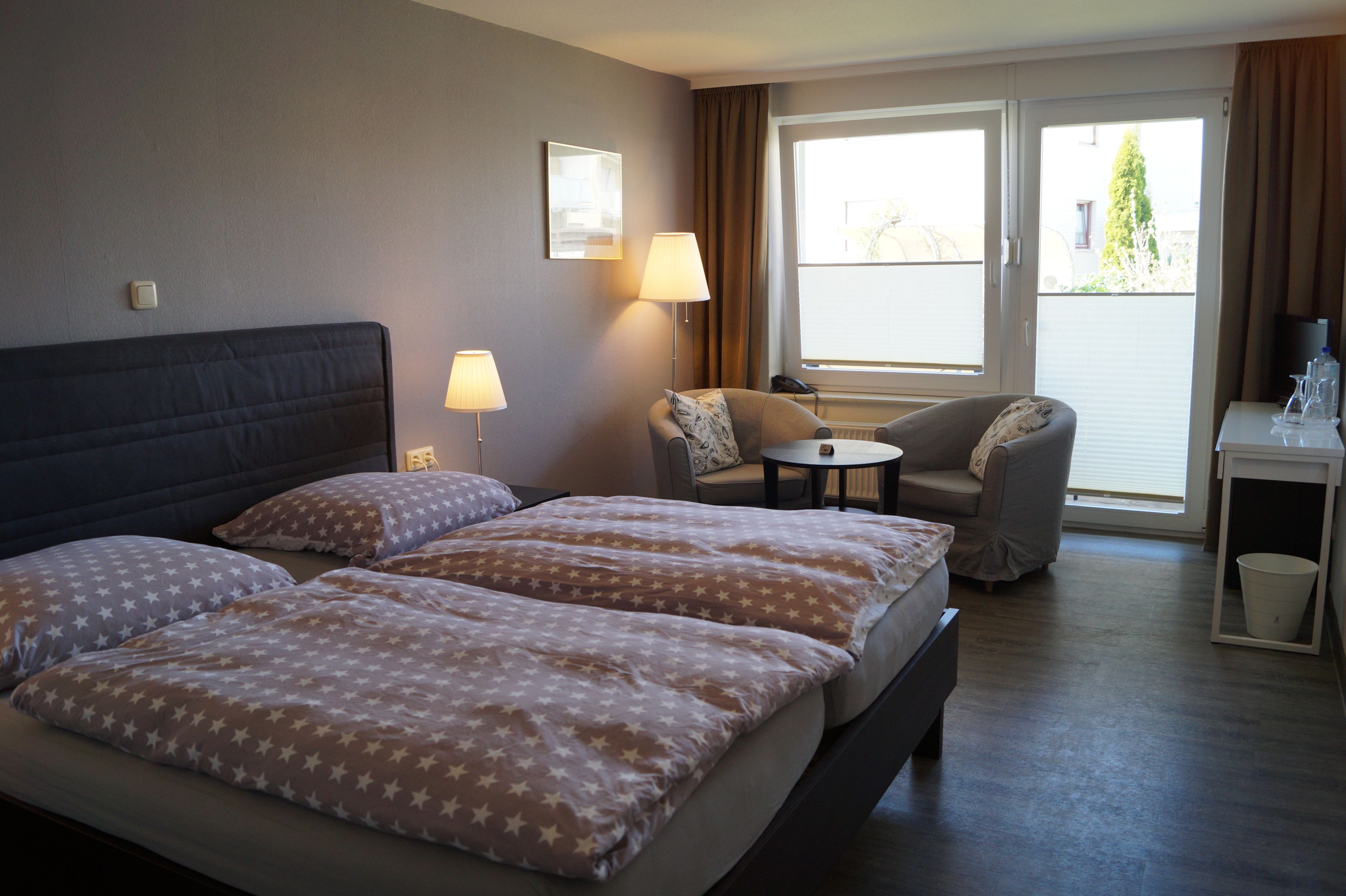 A hotel room with a large bed, two armchairs, a small table, and a window with curtains.
