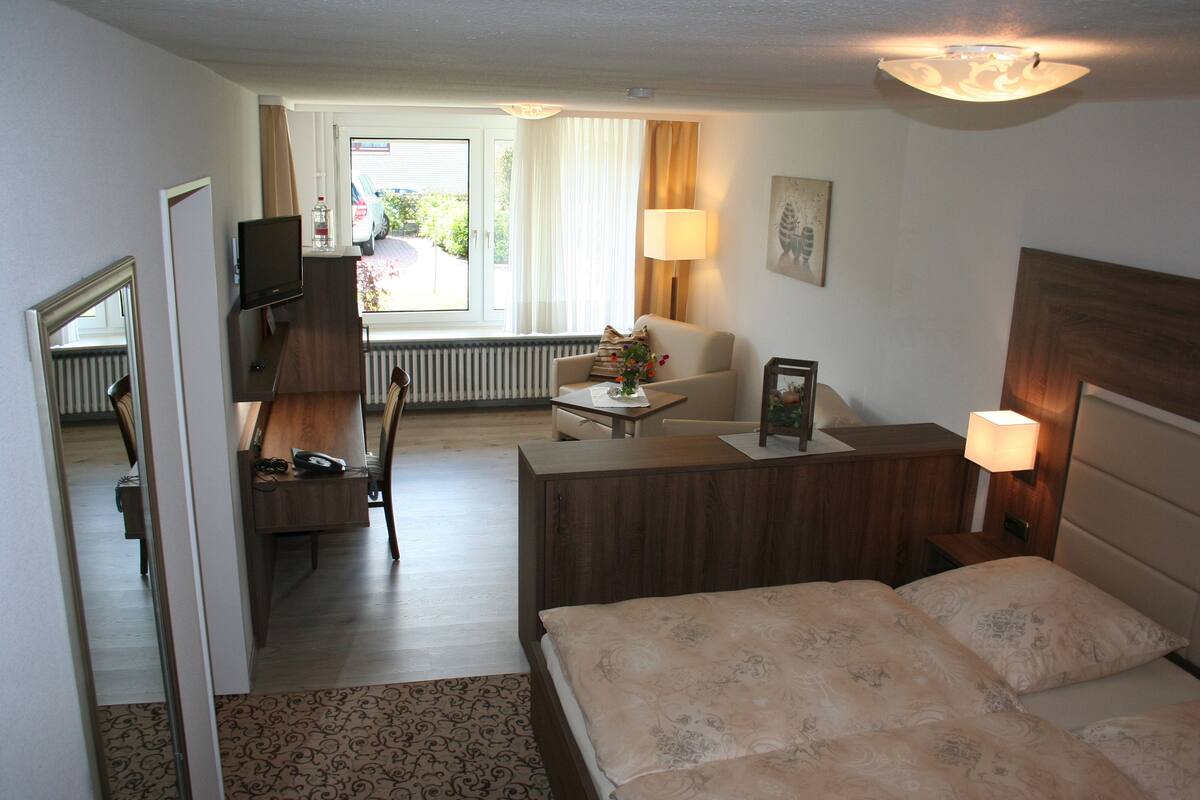 Une chambre d’hôtel avec un lit, un bureau, une chaise, une télévision, une lampe et une fenêtre avec des rideaux.