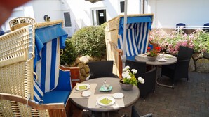 An outdoor patio with wicker furniture, a round table set for dining, and a potted plant. - Hotel Villa Undine (Groemitz)