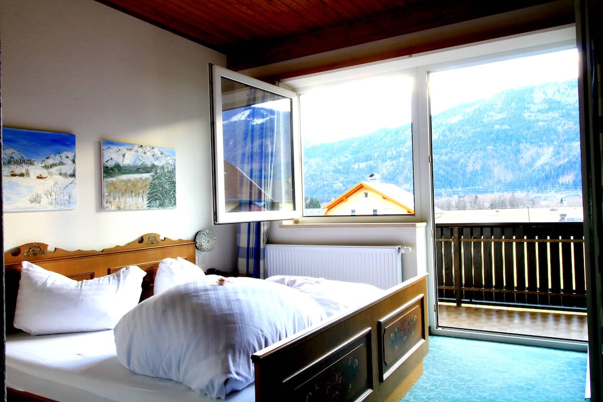 A bedroom with a bed, a window with a view of mountains, and a painting on the wall.